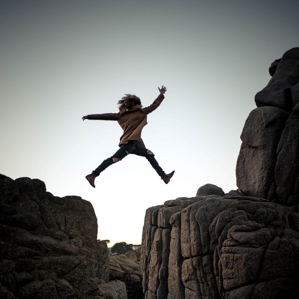 girl jumping across a cliff ridge